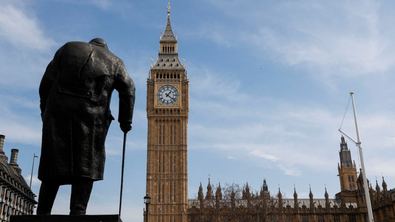The back of the bronze statue of Churchill leaning on a walking stick, with Big Ben and parliament in the background