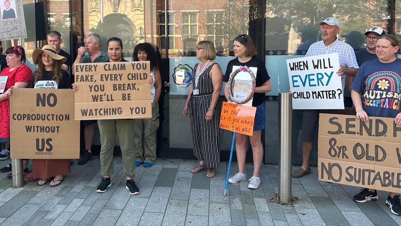 A line of parents outside a council office building hold placards saying with slogans including: "When will every child matter?"