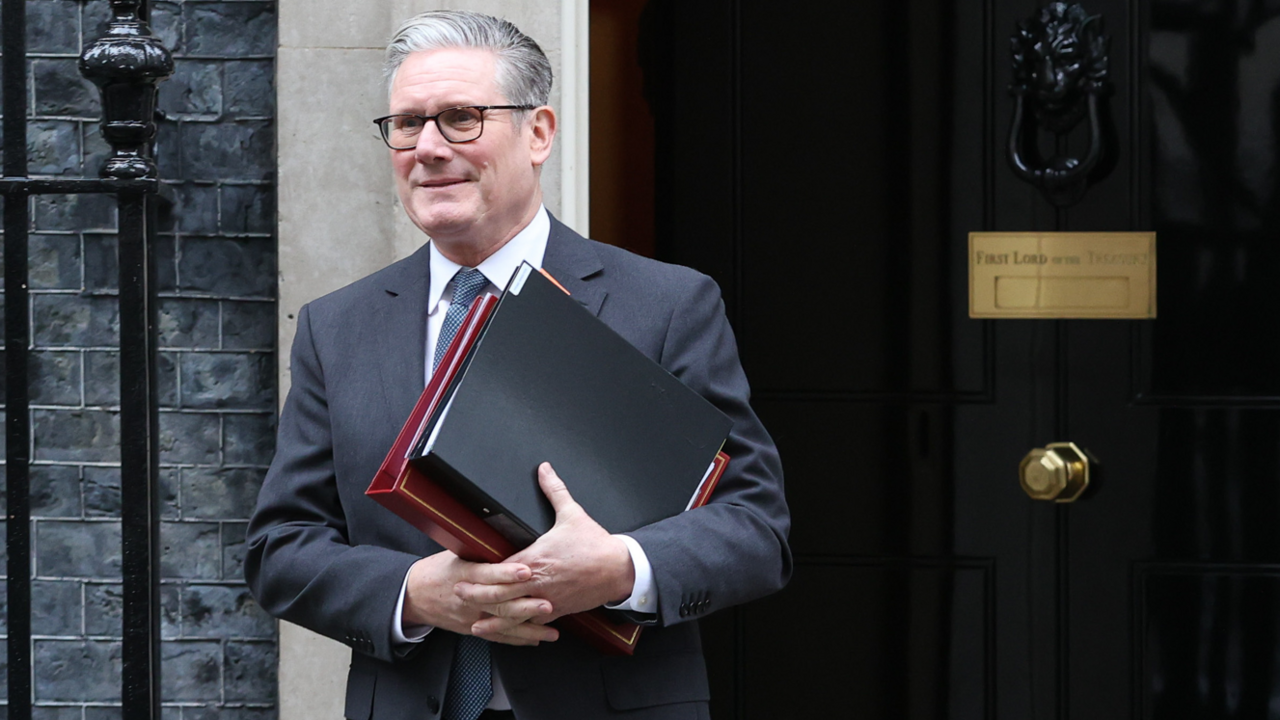 Sir Kier is holding a red and a black file. He's standing outside Downing St. He's wearing glasses and a suit