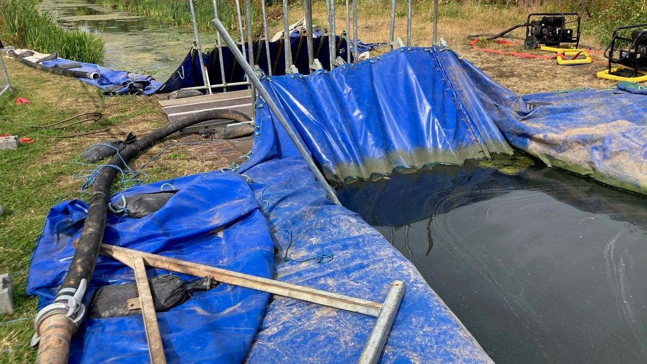 Dam on stretch of Walsall canal, made up of blue plastic sheeting and a framework of metal bars. 