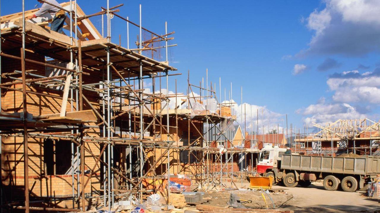 Two partly built homes, surrounded by scaffolding, with a lorry in the background