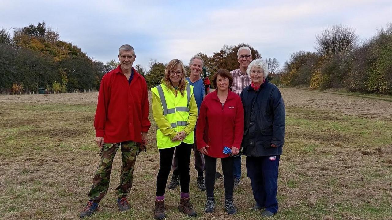 A group of volunteers, in fleeces and hi-vis jackets, stand together in a field.