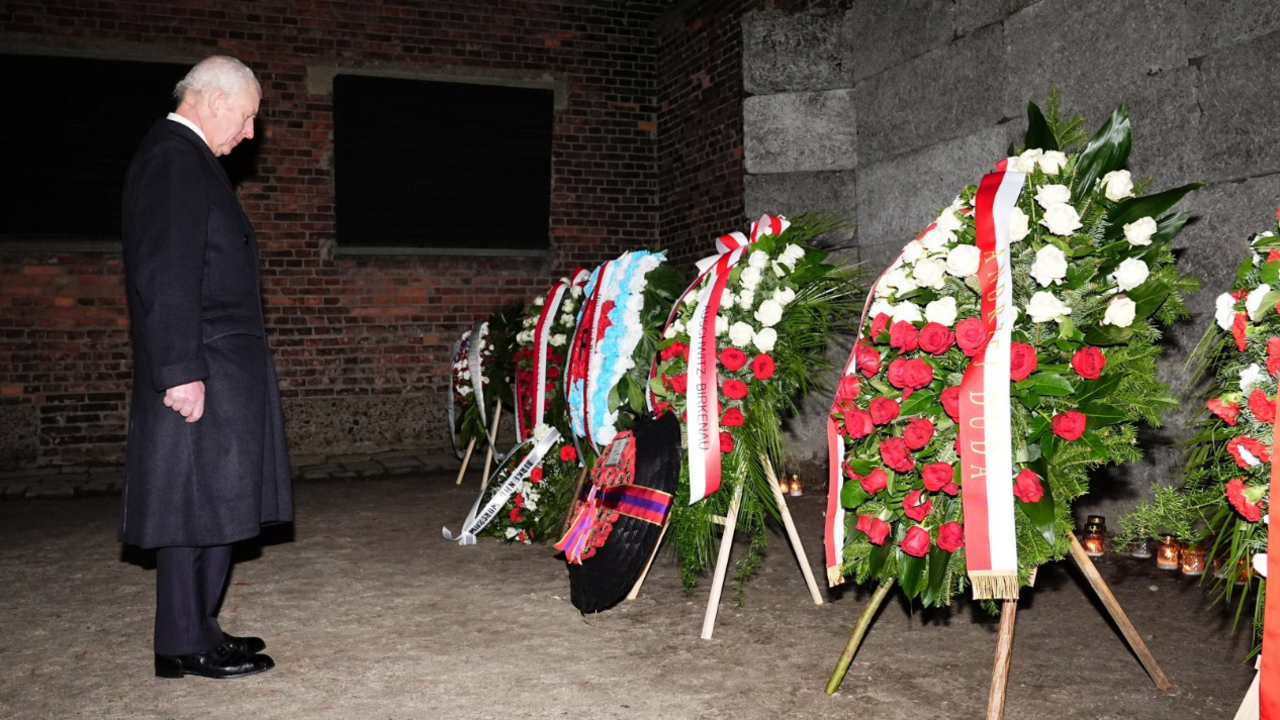 King Charles views floral tributes at 'The Death Wall' during a tour of Auschwitz