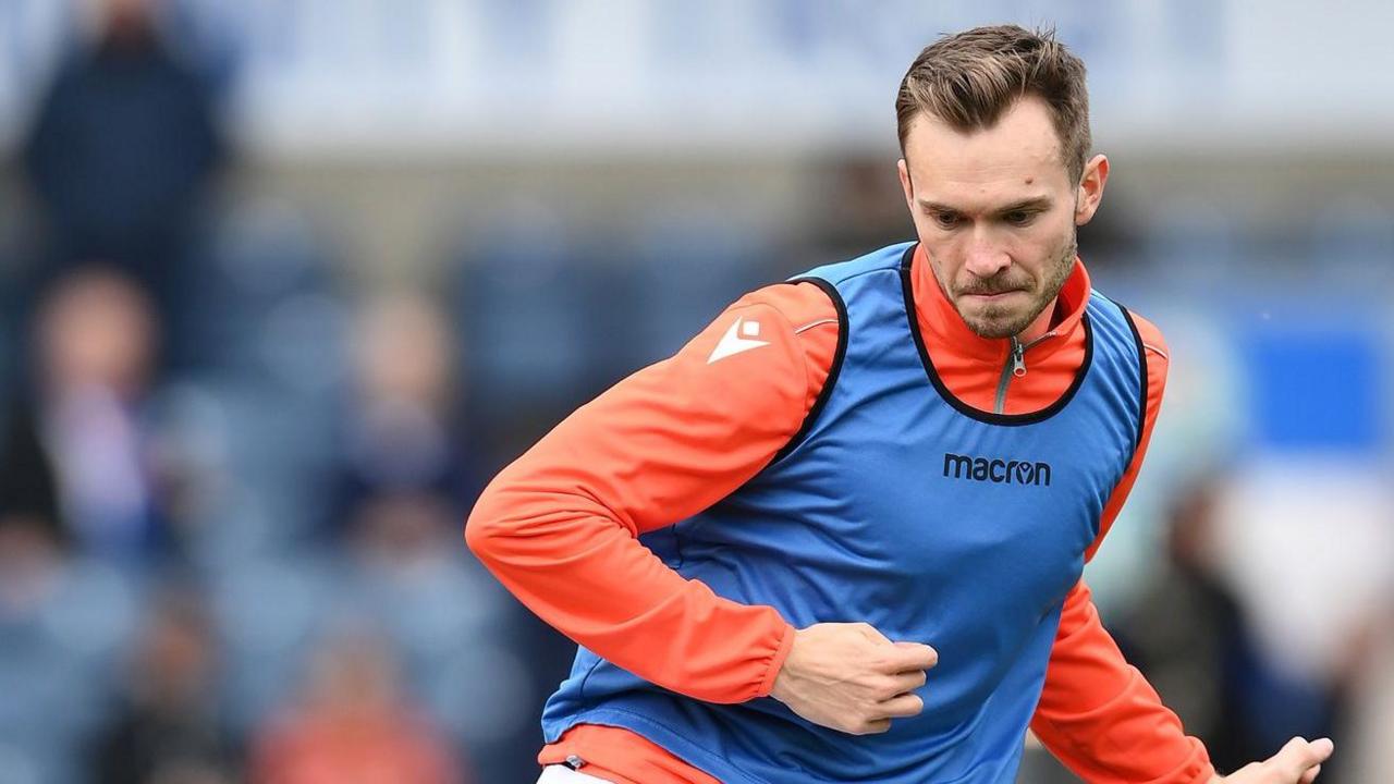 Ryan Hedges, wearing an orange zip-up jacket and a blue vest, warms up for Blackburn Rovers before their game against Southampton in April