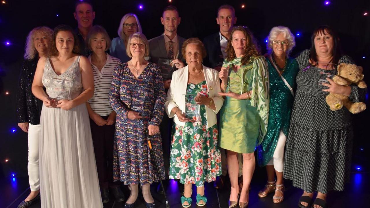 A group picture of all the winners of BBC Radio Solent Make a Difference Awards. They are standing against a wall with purple strobe lights