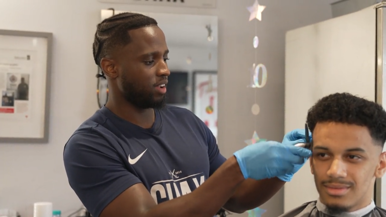 Leeroy Chaxwearing blue latex gloves and cutting a customer's hair.