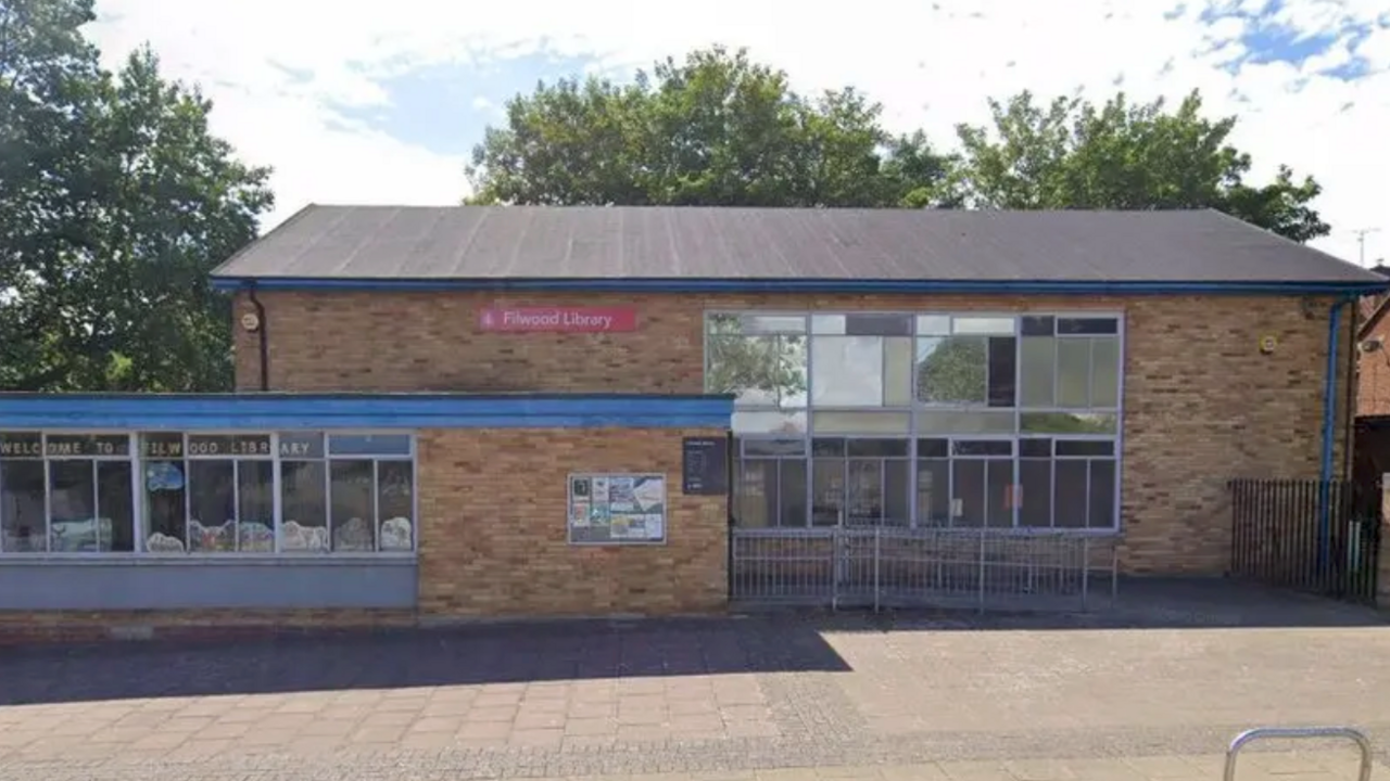 The exterior of Filwood Library in Bristol. It has brown bricks and large windows. There is a silver metal railing leading up to the entrance.