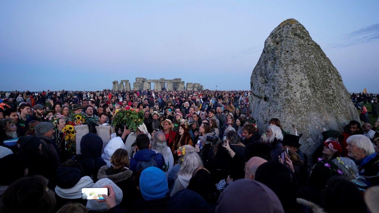 Hundreds of people gather at Stonehenge in Wiltshire during sunrise, as they welcome the Summer Solstice, standing around a stone, with more stones in the background
