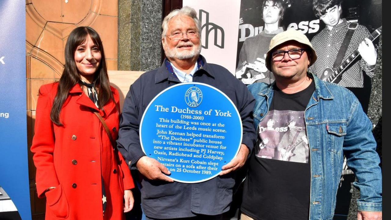 Amanda Burns, John Keenan and Paul Cockroft outside the venue, with Mr Keenan holding the plaque.
