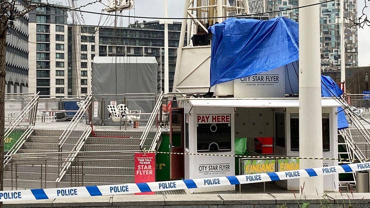 A shot of the ride in daylight, showing white plastic seats at an angle with chains twisted together, and the entrance to the ride in the foreground that's been covered up with tarp. The area is cordoned off with police tape.