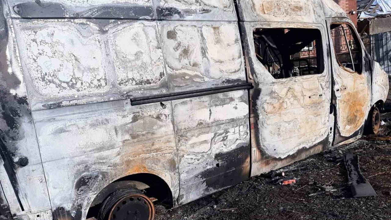 A damaged white van on a black burnt ground.