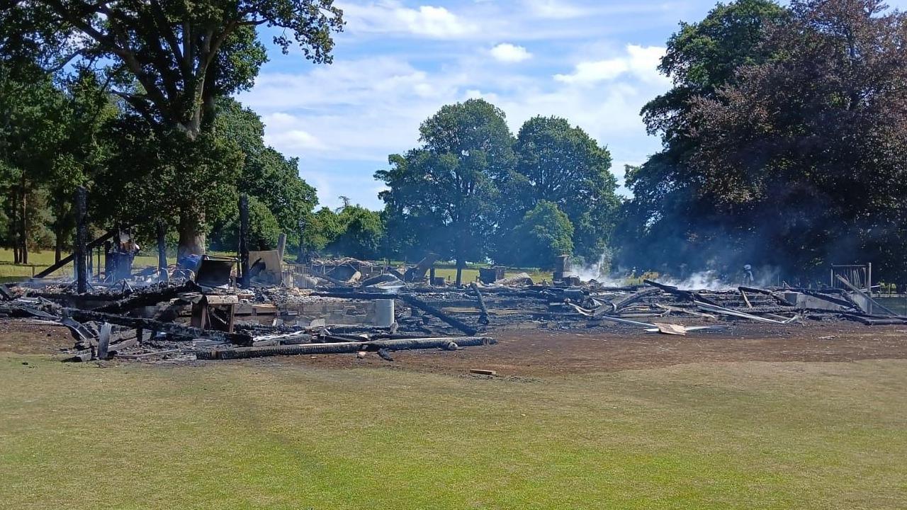 Smouldering remains of the wooden clubhouse surrounded by green fields and trees