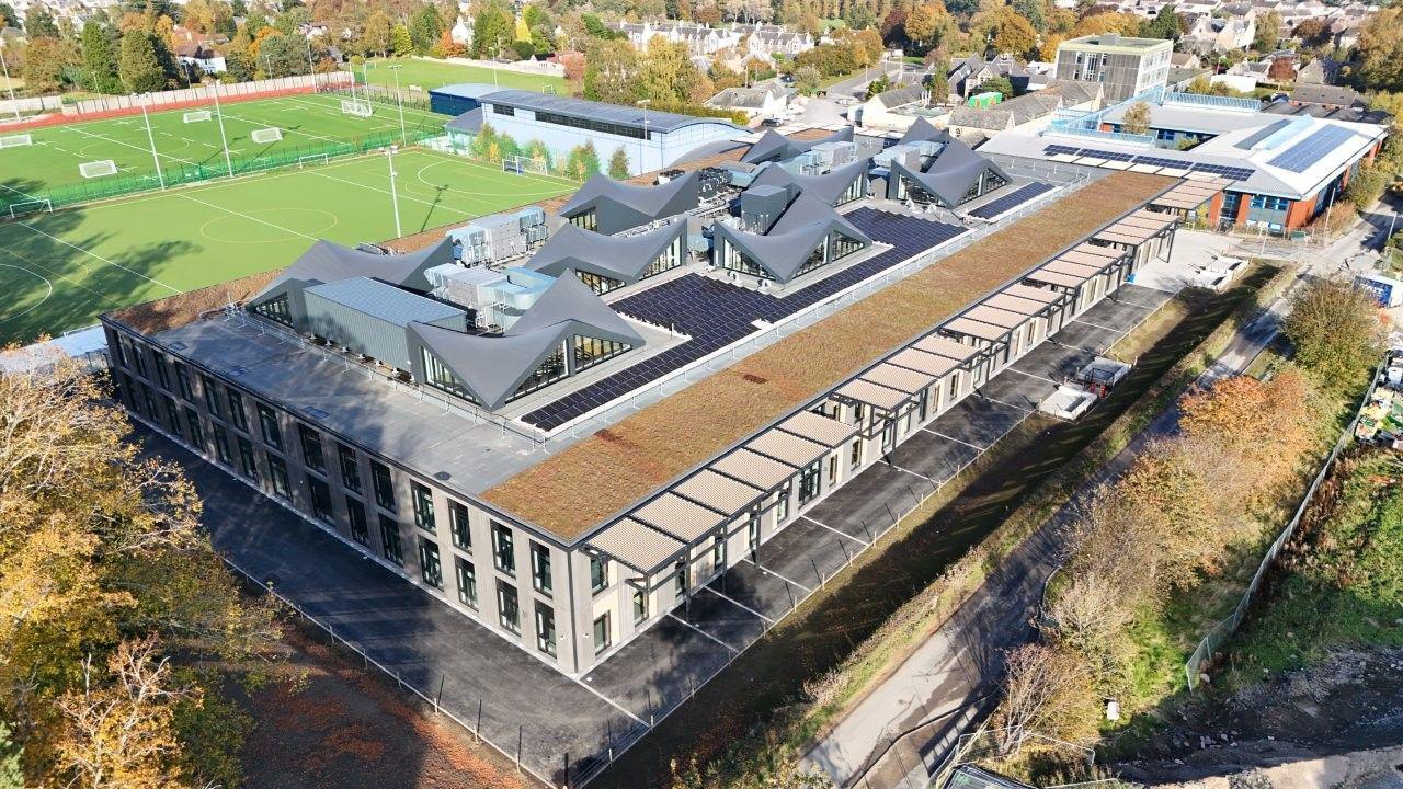 The new Peebles High School building viewed from above with pointy sections to its roof and sports pitches in the background
