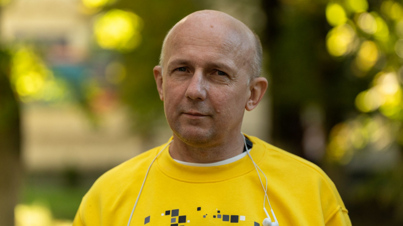 Dmytro Khyliuk stands looking into the camera, wearing a yellow shirt and headphones