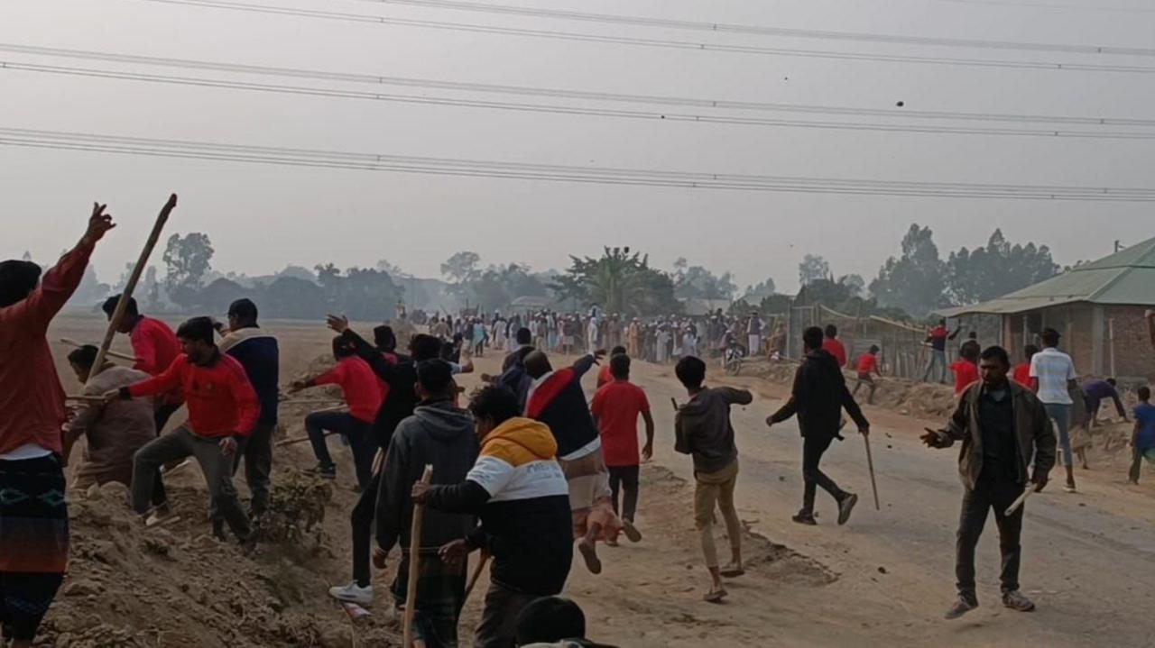 In Dinajpur, men, some holding sticks, throw objects at another group in the distance