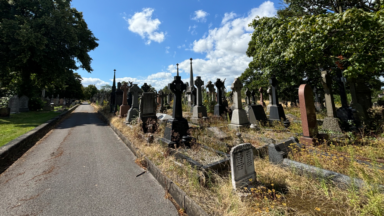 A general view of Rock Cemetery in Nottingham showing gravestones on the right of the frame, taken from a footpath alongside.