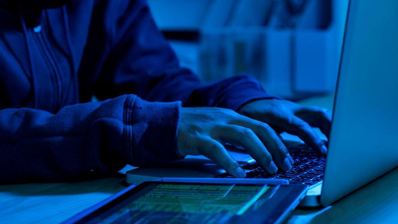 A blue-lit room with a person in a hoodie typing on a laptop