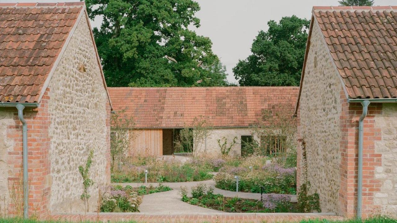 A group of single storey stone buildings around a garden with meandering paths and beds planted with ornamental grasses and flowers with a pink and purple hue