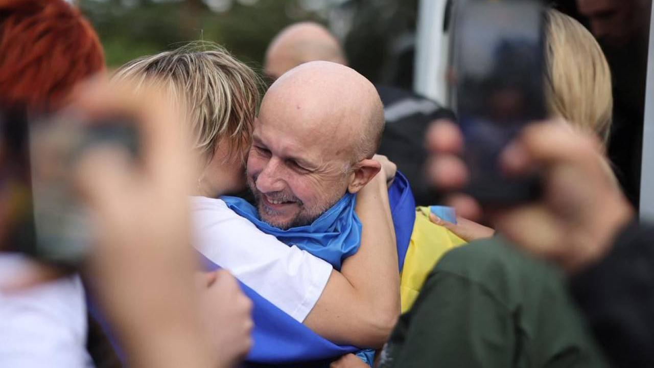 The moment Dmytro Khyliuk was freed. The photo shows Dmytro hugging someone, while draped in a Ukrainian flag, with a big grin on his face