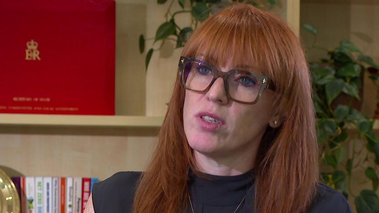 Angela Rayner, a woman with long ginger hair and glasses, against a backdrop with a ministerial red box on a shelf