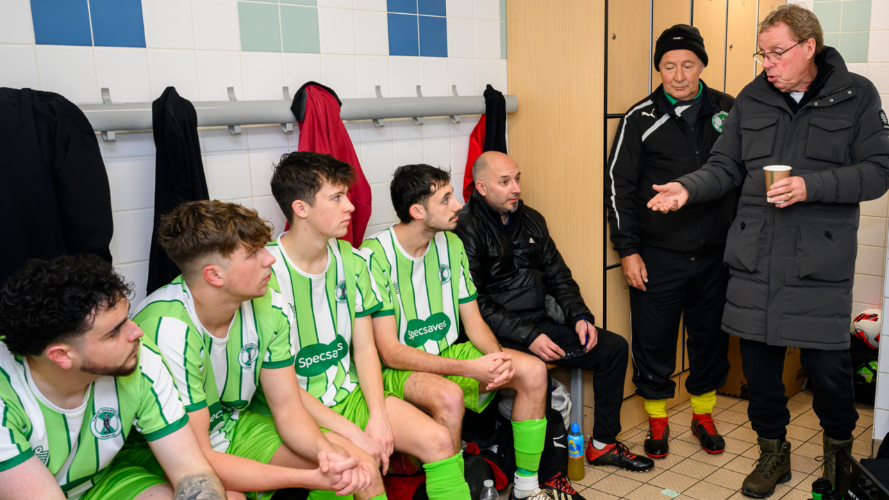 Harry Redknapp in a changing room talking to several footballers sitting on a bench, wearing their green and white striped Specsavers kit