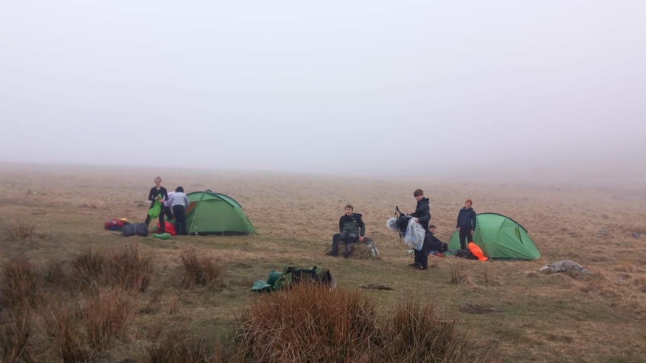 A group of people putting up green tents and setting up camp in the middle of the moor.