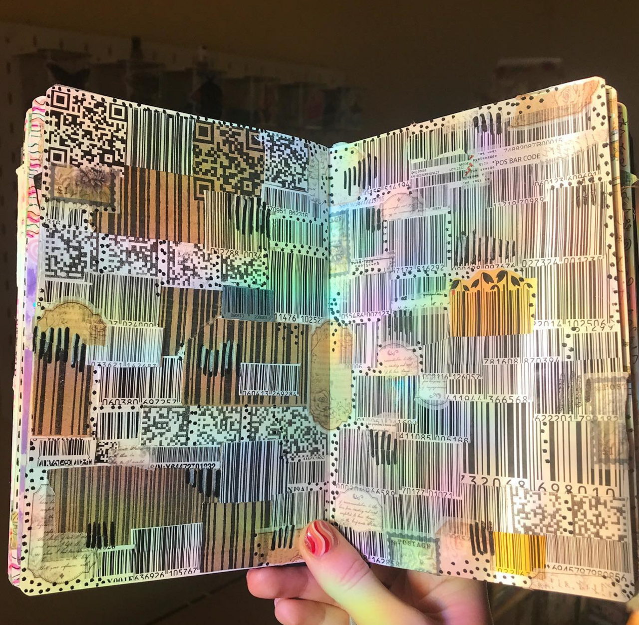 Two pages of a book are being held open with a hand. They are iridescent barcodes and QR codes covering the whole page.