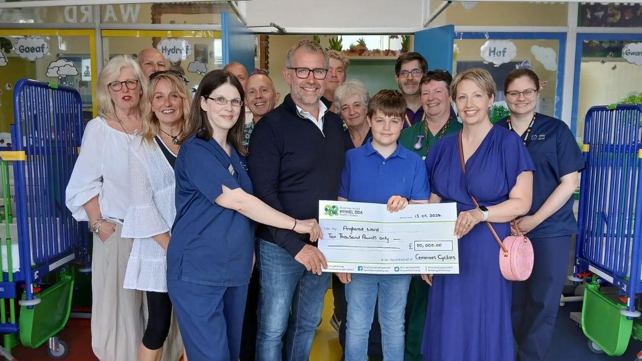 A group of smiling people presenting a large cheque for £10,000 in a children's ward