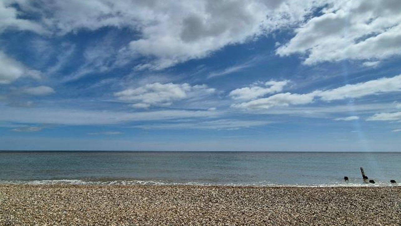 Looking out at a calm sea across a pebble beach beneath a sky with fairweather clouds