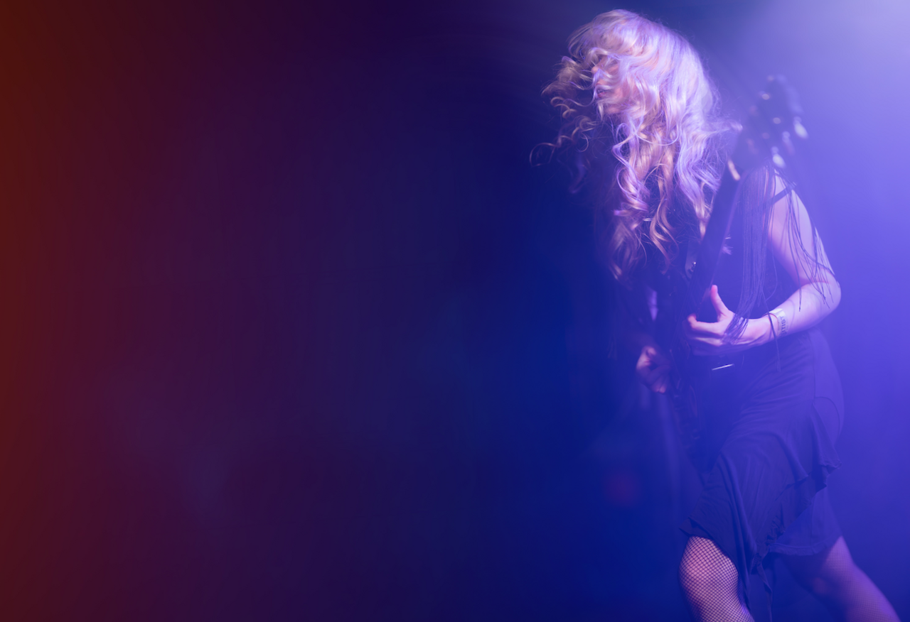 Meatdripper guitarist Liv Barlow has long blonde hair and is wearing a dark dress. Her hair floats about her head as she plays guitar