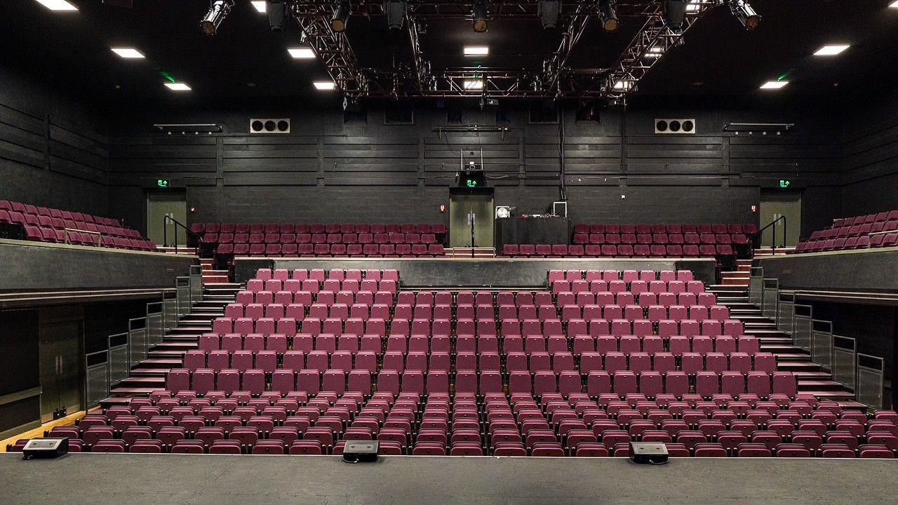 An empty theatre stadium with red chairs lined and bright lights on the stage 