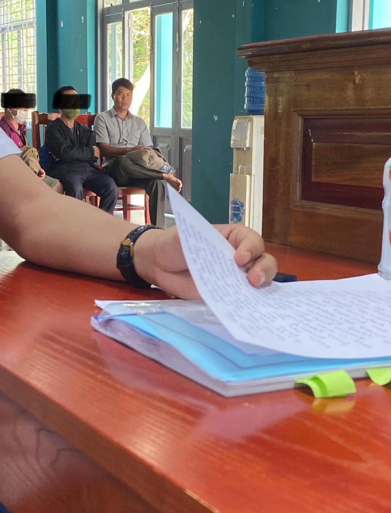 Documents on a table with two detainees in the background next to a Vietnamese police officer.