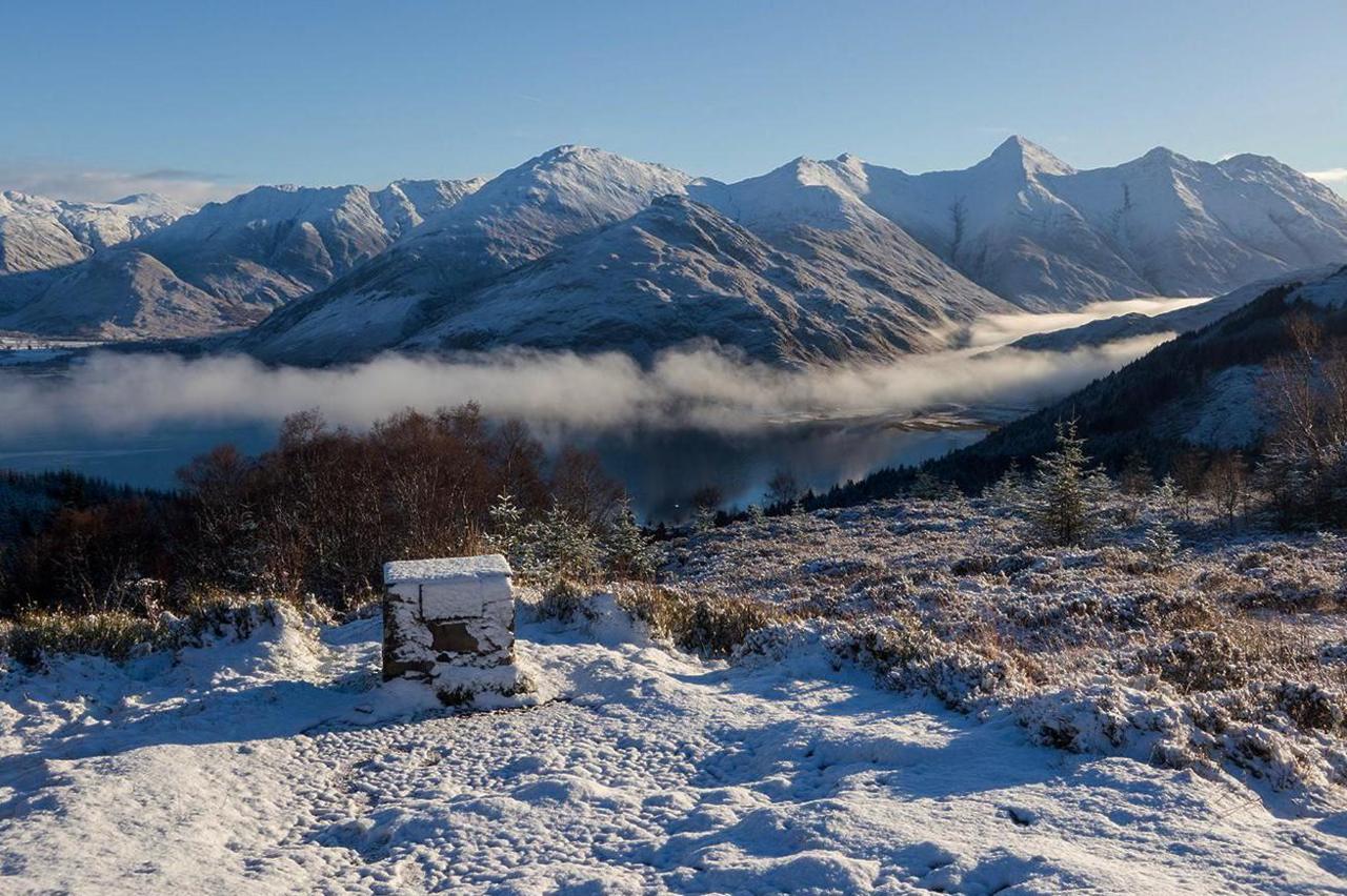 A viewpoint overlooking snow-covered mountains and low cloud drifting over a loch.