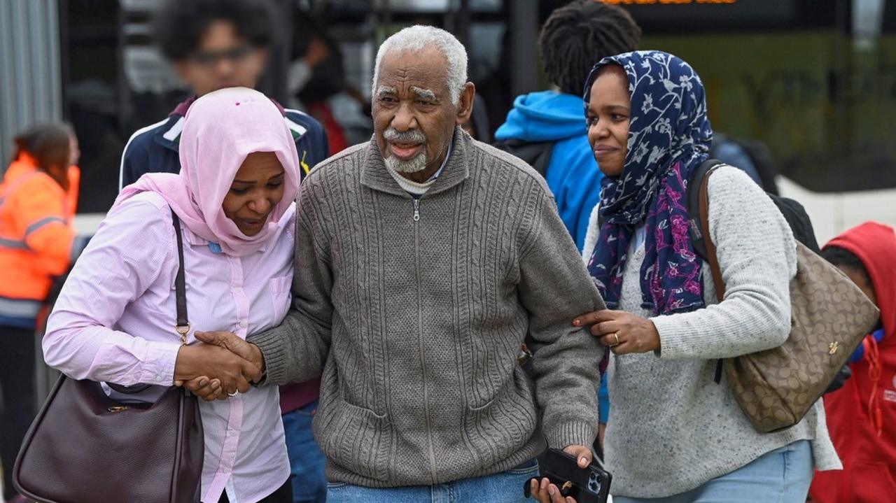 Two women flank an older man as they arrive off a bus