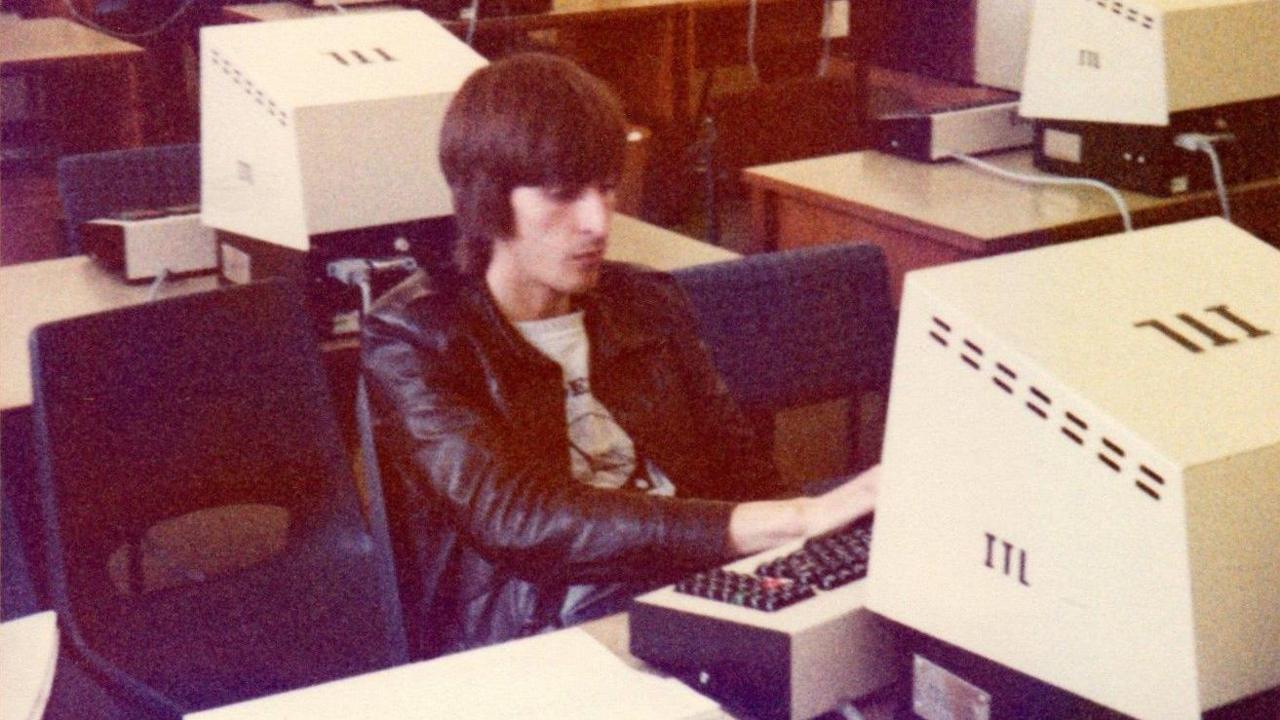 A young man sits in a 1970s computer lab.