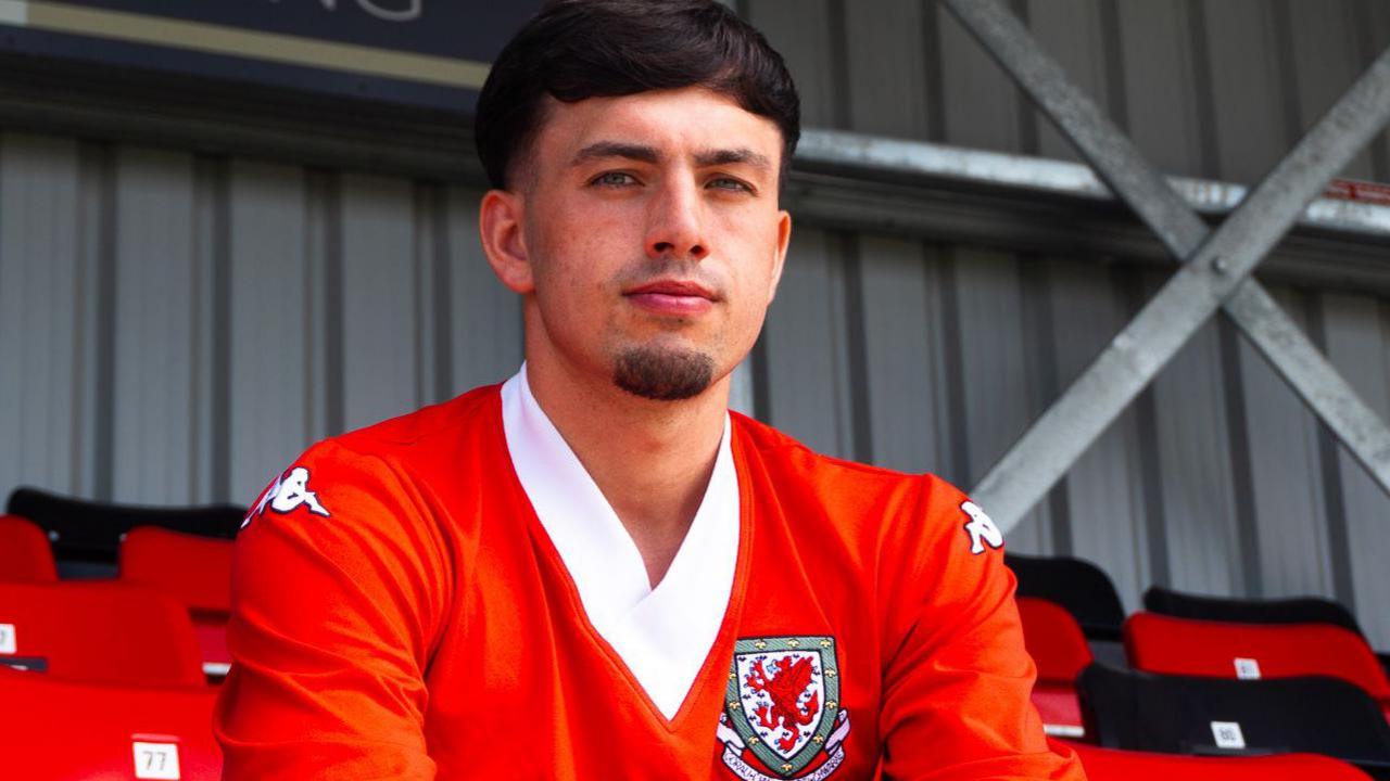 Tom Tweedy sitting in a football stand wearing a Wales football shirt