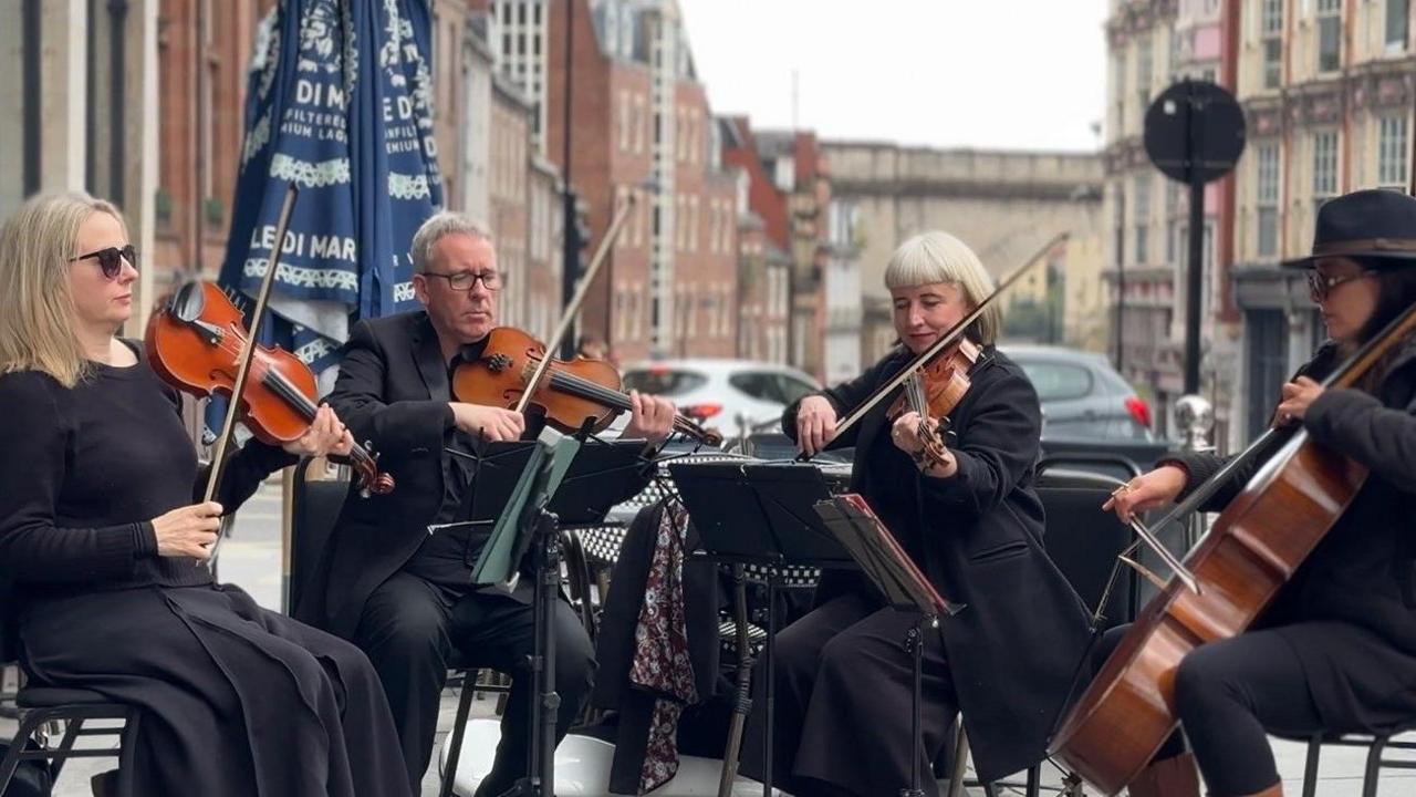 A string quartet, of three women and one man, all dressed in black performs during the event. 