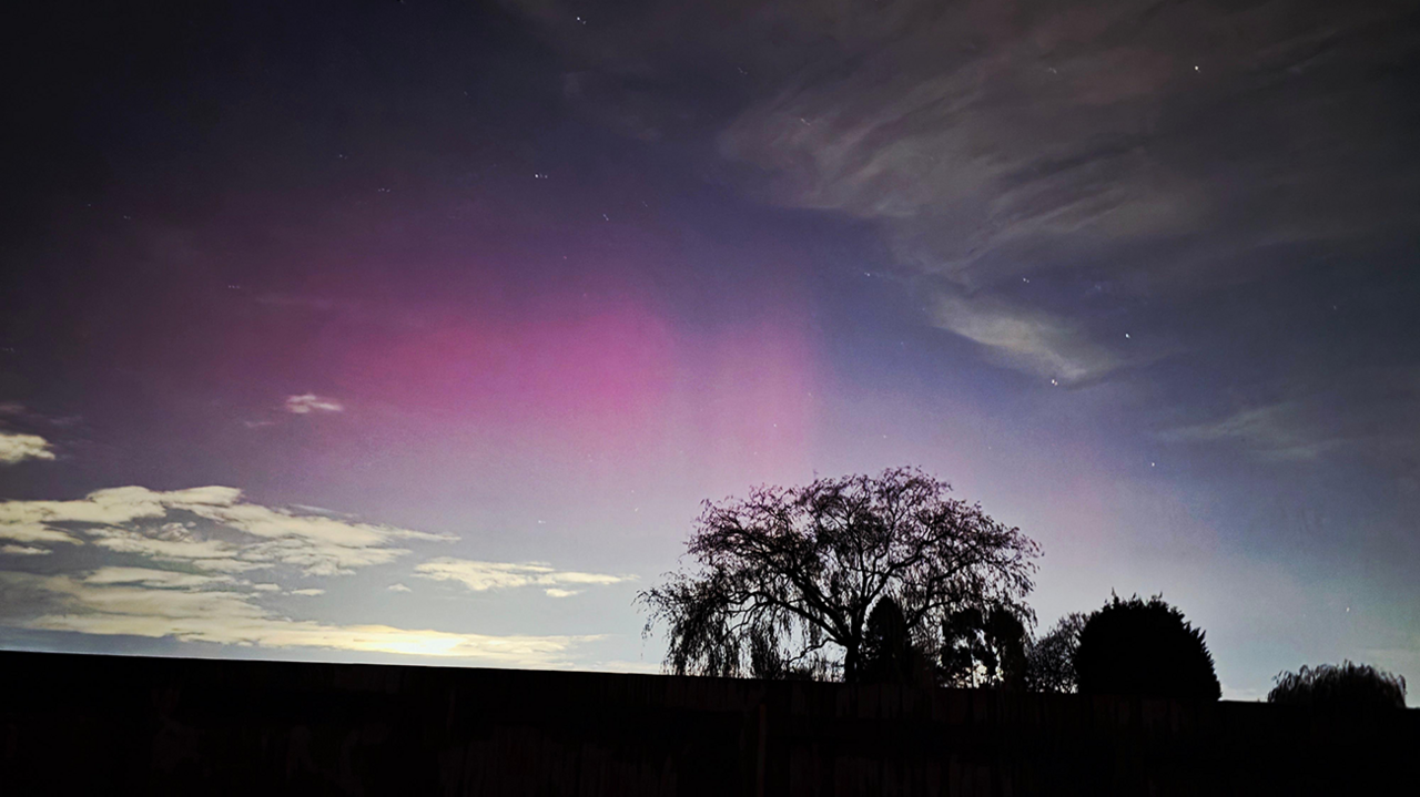 A field and a handful of trees are in silhouette at the very bottom, with the evening / early morning sky dominating the scene in Romsley. A pink glow is in the centre, with a few clouds to the top right and bottom left