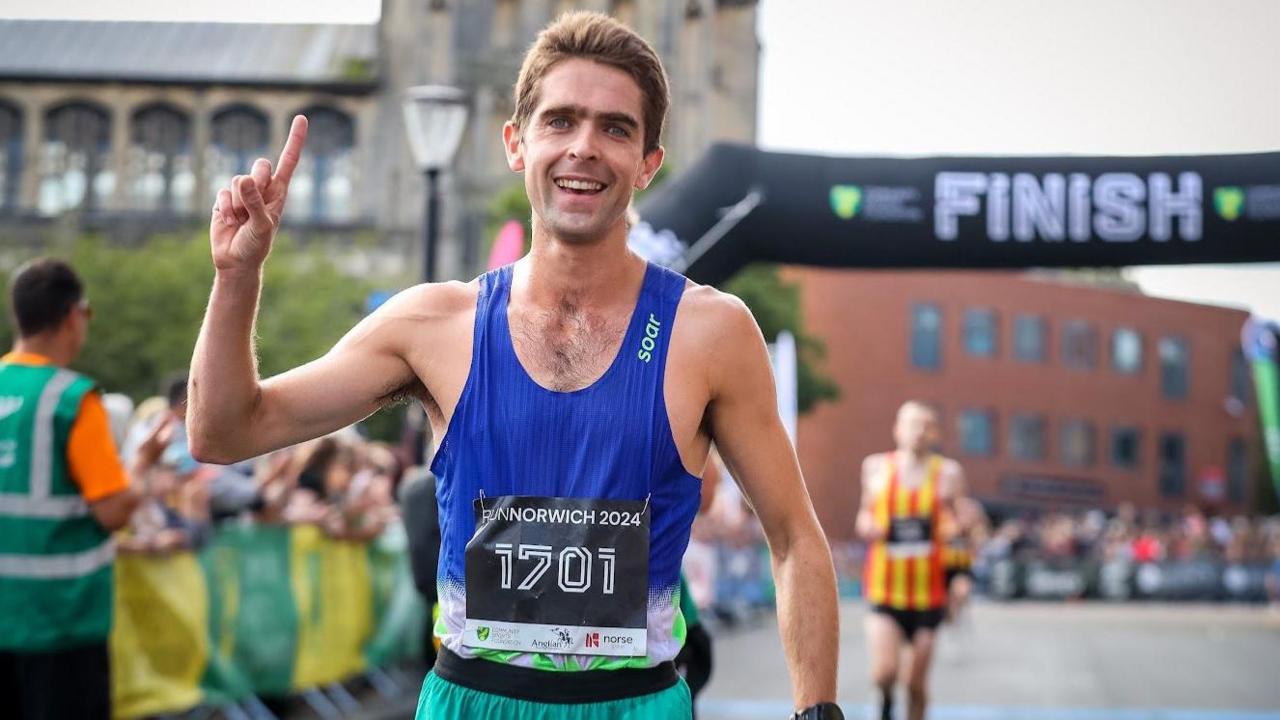 Jonathan Escalante-Phillips wearing a blue vest at the finish line pointing to the sky