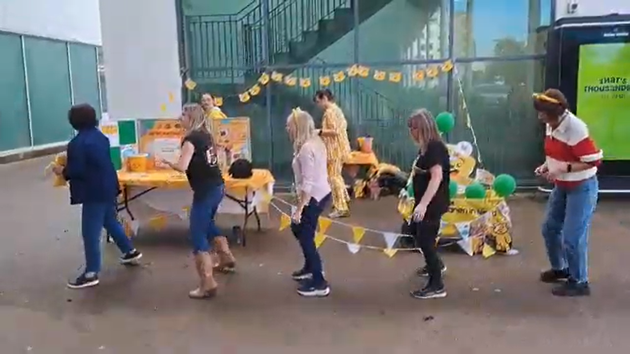 Five people line dancing in front of a yellow Children in Need stall