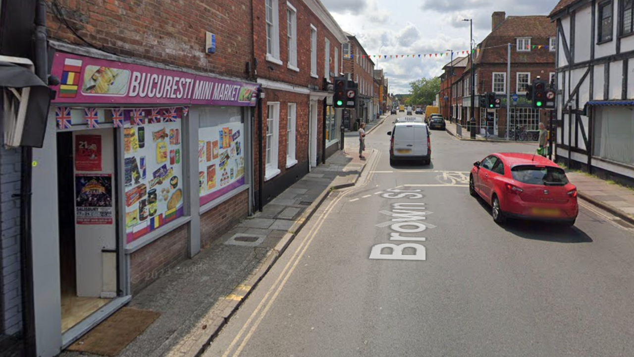 Google maps image of a street in Salisbury. Bucuresti Mini Market is on the left - it has union jack bunting and a pink storefront. Pictures of various food and drink products can be seen on the windows. Traffic lights and other buildings can be seen along the street.  