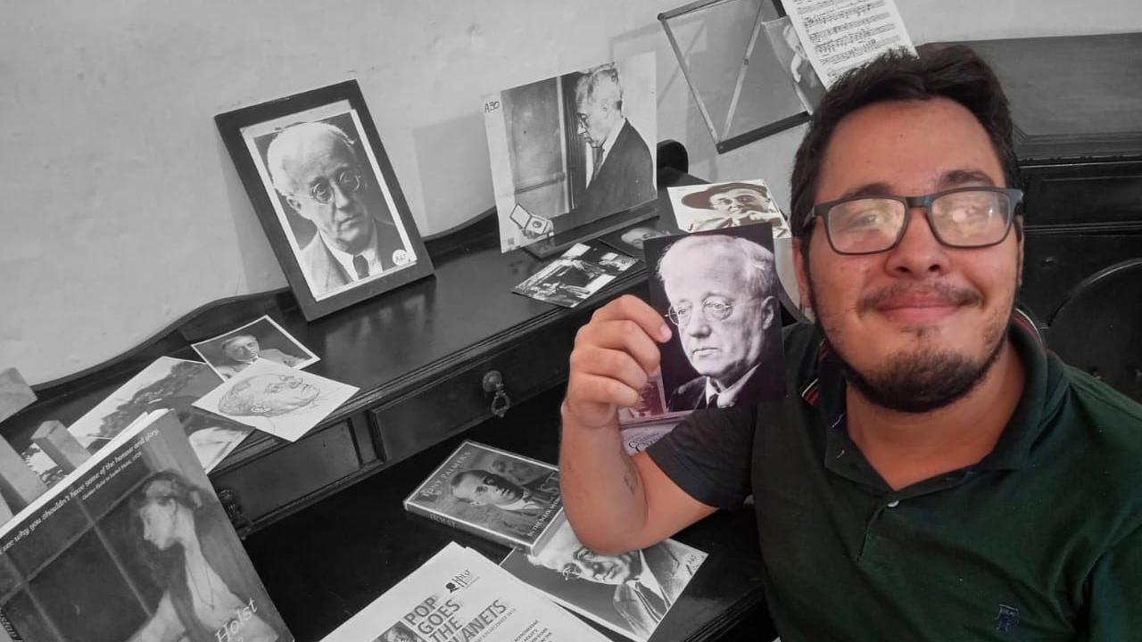 Bruno Lima sitting at a desk covered in pictures of Gustav Holst