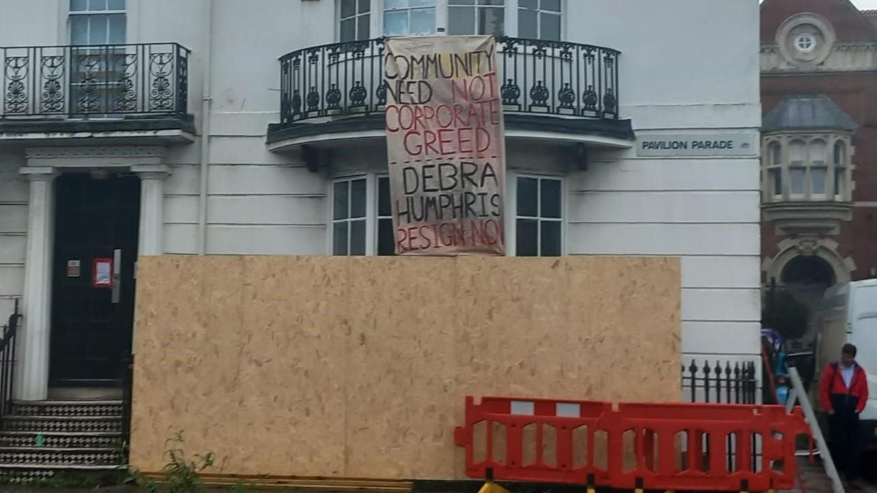 The building in Pavilion Parade, boarded up with a wooden board and a banner calling on the vice chancellor, Debra Humphris, to resign