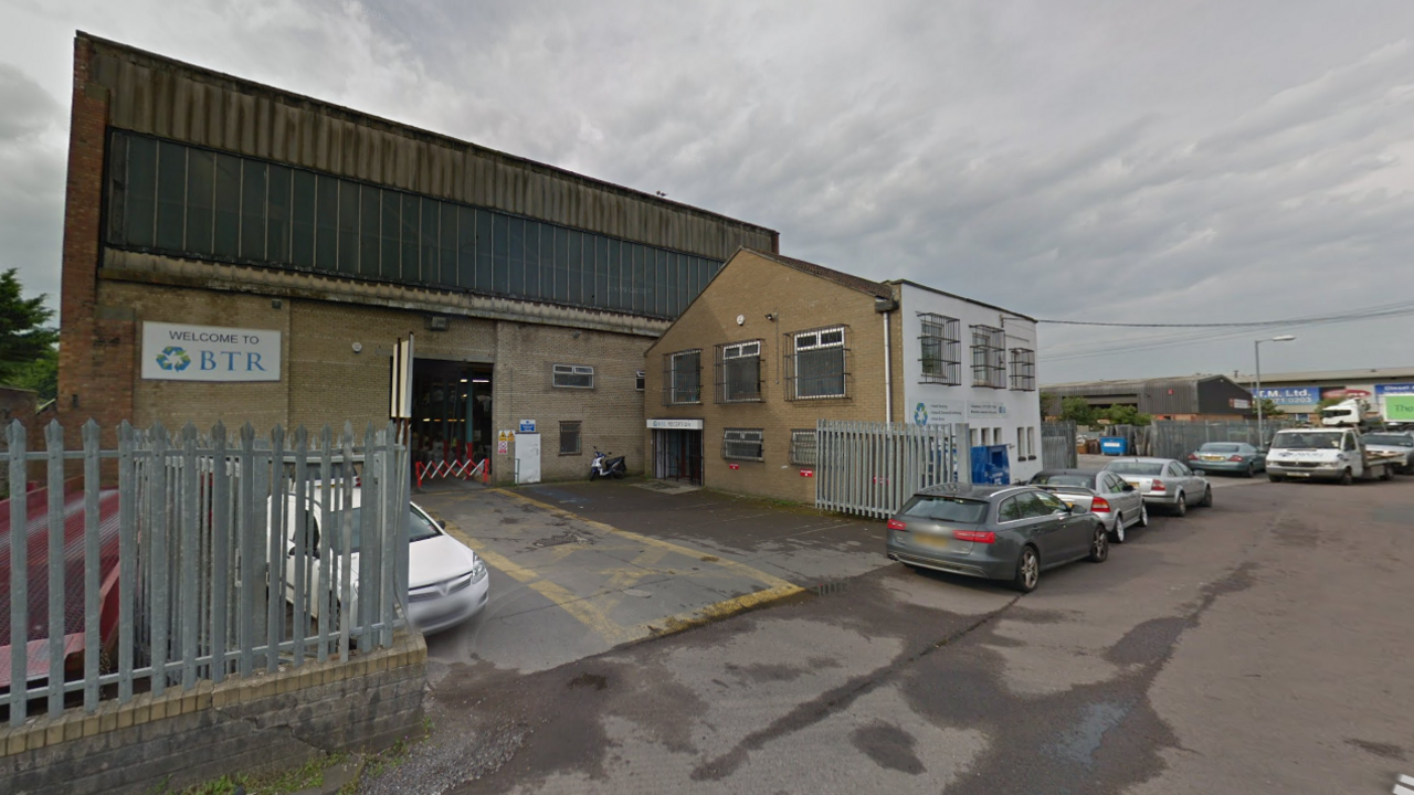 A warehouse in an industrial estate with cars parks along side its front buildings.