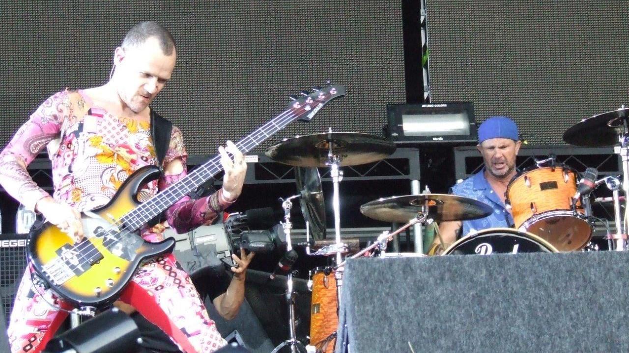 Members of Red Hot Chili Peppers perform at Portman Road stadium. One member plays a bass guitar while another performs on the drums behind him.