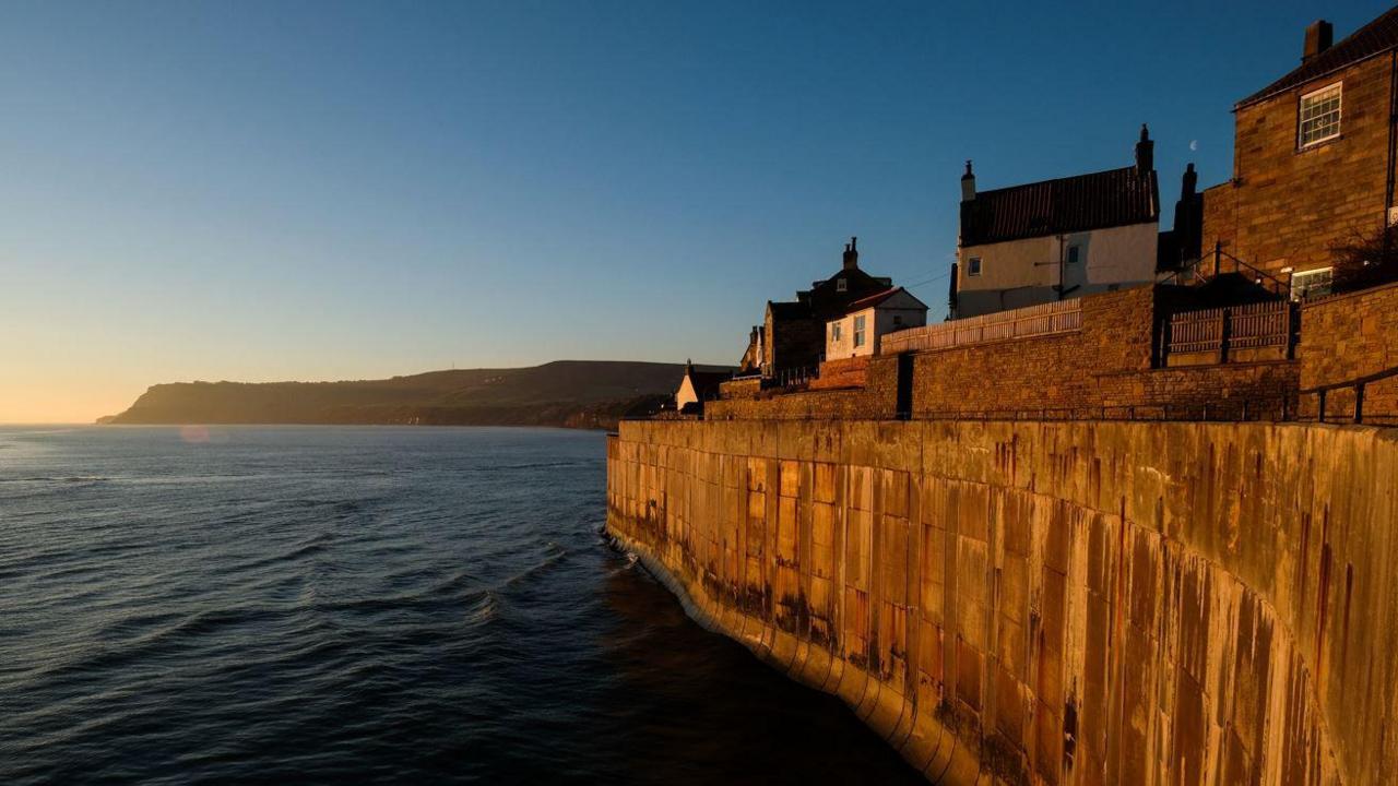 Buildings at Robin Hood's Bay, pictured alongside the sea and cliffs at sunset 