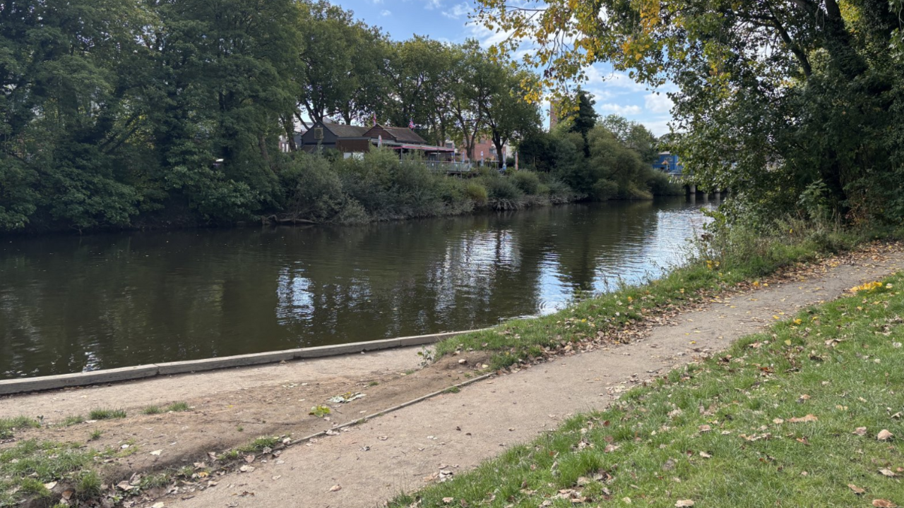 The river near Shrewsbury. There are trees either side with a house on the left hand side. A path can be seen on the right side of the image.
