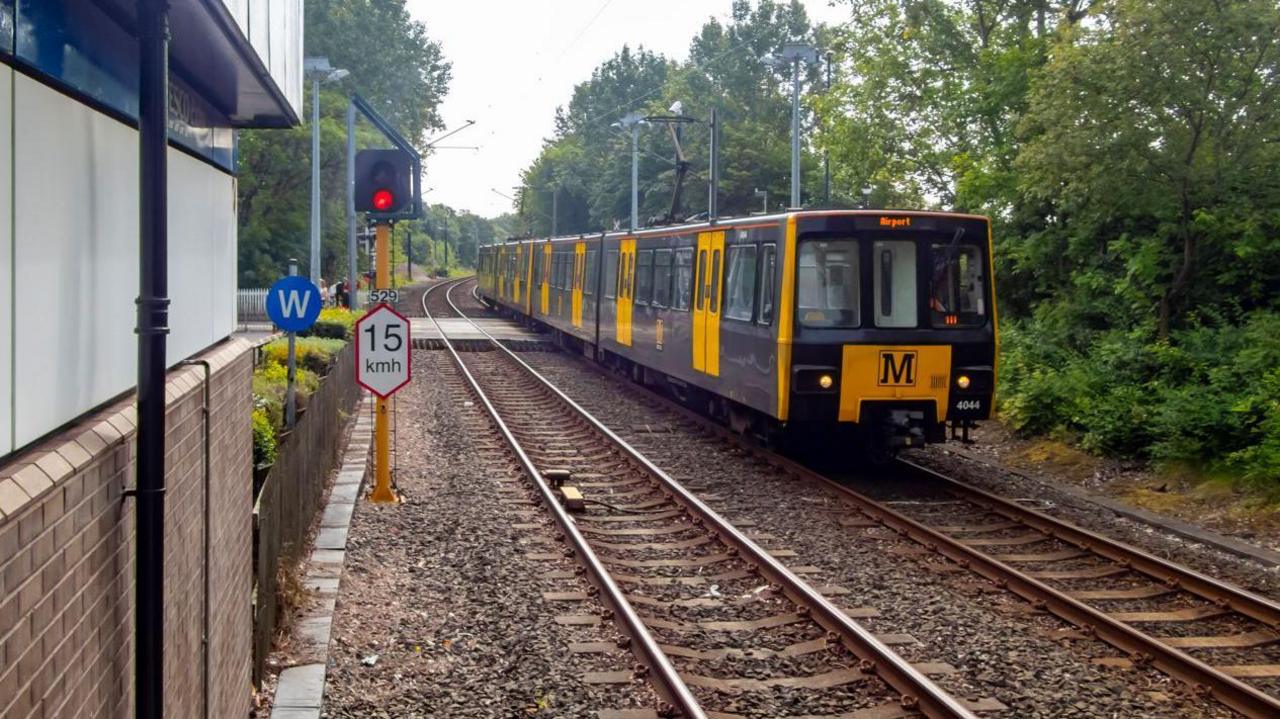 A Tyne and Wear Metro train. The train is travelling on the right hand side tracks towards the camera. A signal light showing red is on the left above a 15kmh speed limit sign.