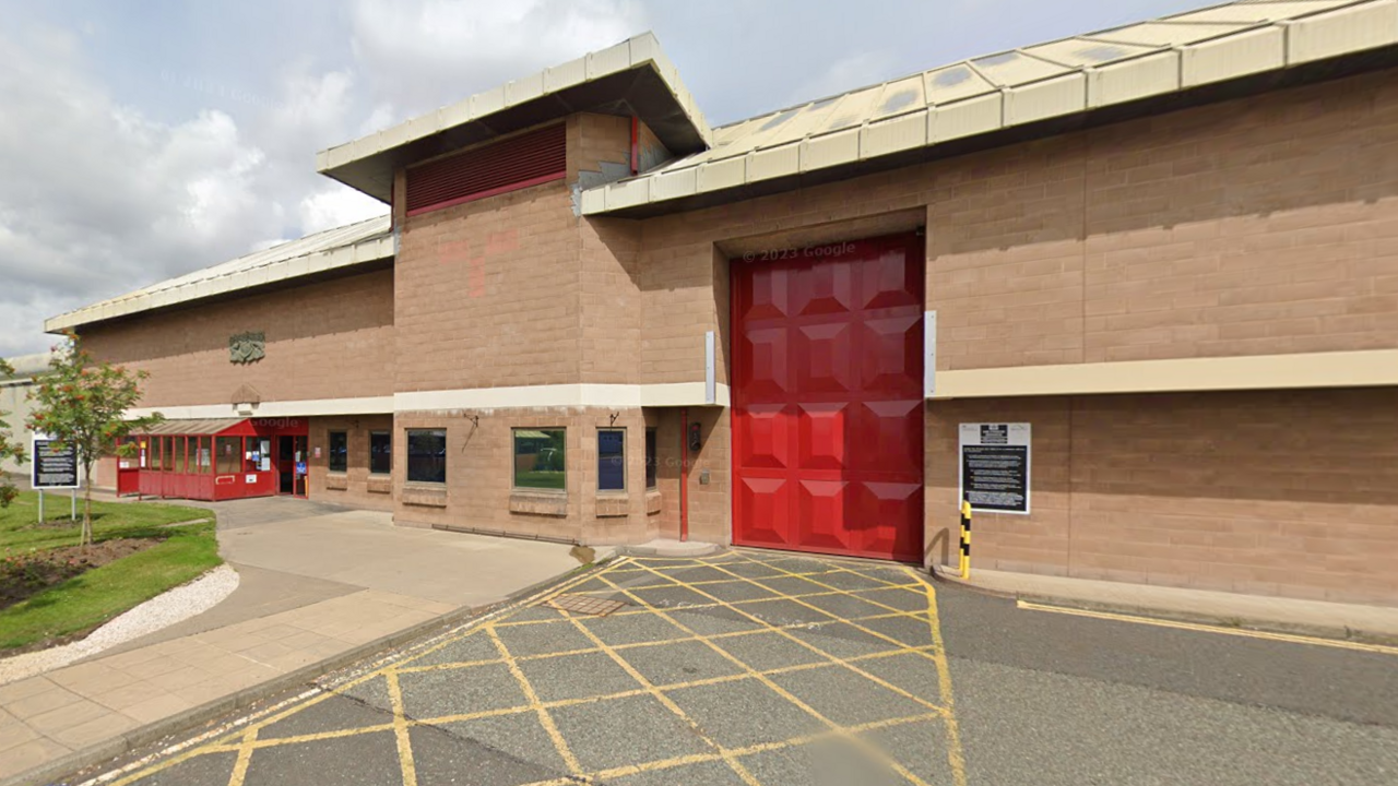 The outside of Holme House Prison which is a large brick building with a big red gate and smaller entrance to the left.