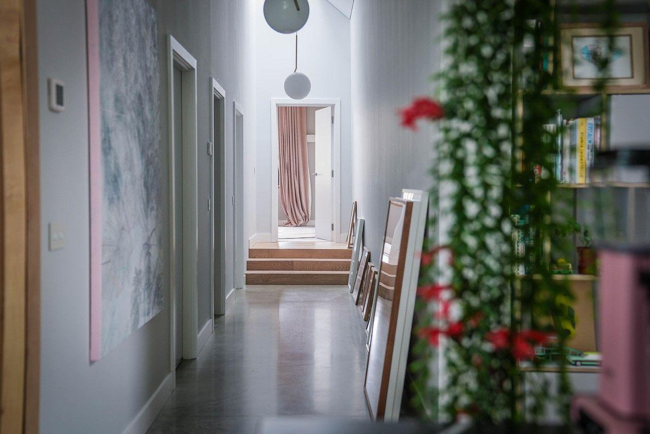 The view down the hallway, with white walls and doors, and paintings and framed images with pale pink tones along the wall